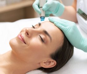 Close up of calm relaxed lady lying with her eyes closed and professional cosmetologist cleaning her skin with dermabrasion tool